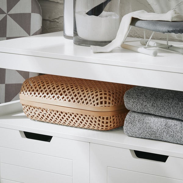 Detailansicht eines weißen Badezimmerschranks mit Wäschekorb, Handtüchern und Waschpulver