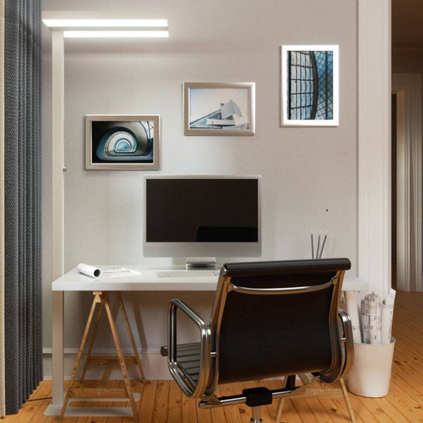 Moderner, heller Arbeitsplatz mit Schreibtisch auf Holzböcken, Bürostuhl, Monitor, Stehleuchte und gerahmten Architektur-Bildern.