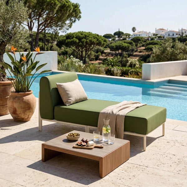 Grüne Polster-Gartenliege mit Kissen und Decke neben einem Pool sowie niedriger Loungetisch in Holz- und Steinoptik.