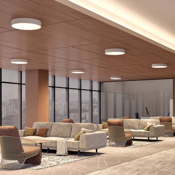 Runde flache LED-Deckenleuchten an einer Holzdecke in einem modernen Bürobereich mit Sofas und Stadtblick.