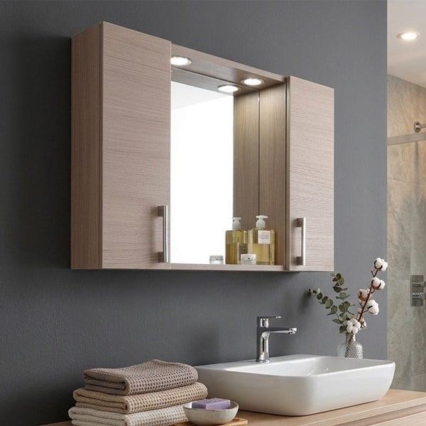 Moderner Badezimmer-Spiegelschrank in Holzoptik mit zwei Seitentüren, Metallgriffen und integrierter Beleuchtung über dem Spiegel.