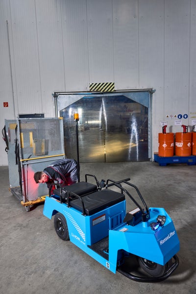 HanseLifter Elektroschlepper im Lager beim Ziehen eines Gitterwagens. Ein Mitarbeiter prüft die Verbindung.