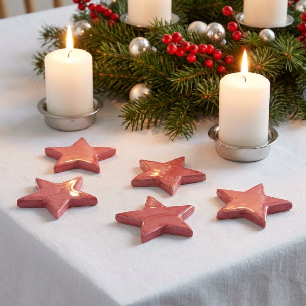 Fünf dekorative Weihnachtssterne aus Keramik als Tischschmuck arrangiert vor einem Adventskranz mit brennenden Kerzen auf einer Tischdecke.