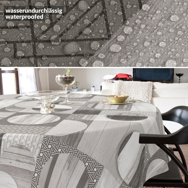 Wasserundurchlässige, runde Tischdecke mit grauem geometrischem Muster aus Kreisen und Holzoptik auf einem Tisch in einem hellen Wohnzimmer.