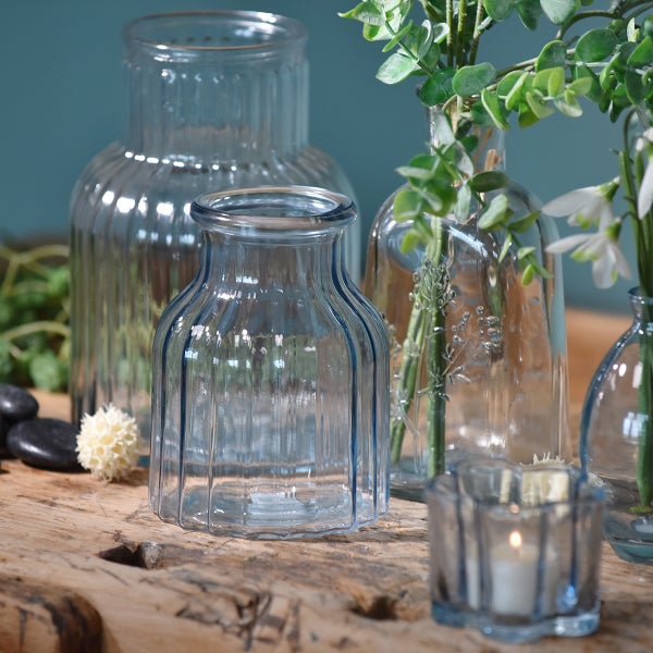 Set aus geriffelten Glasvasen und einem Teelichthalter auf einem rustikalen Holztisch, dekoriert mit Pflanzen und Steinen.
