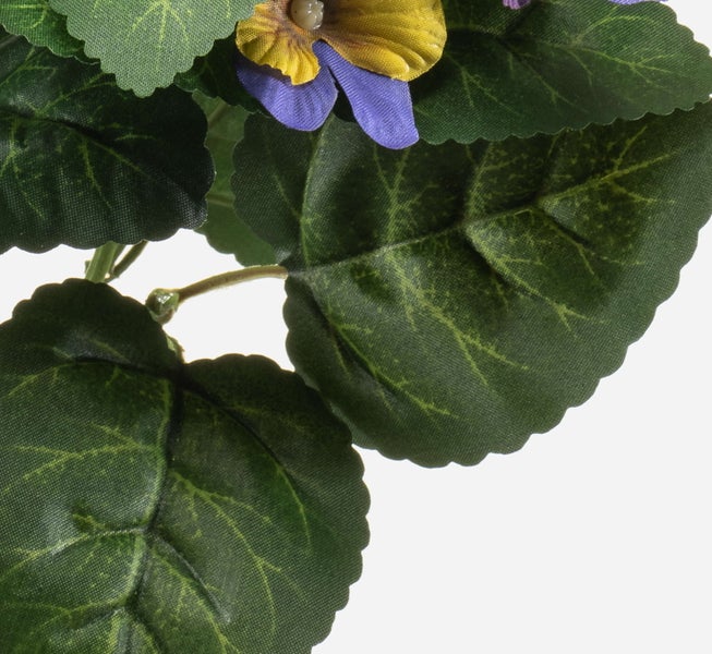 Detailaufnahme einer Kunstpflanze mit grünen Blättern und einer gelb-violetten Blüte.