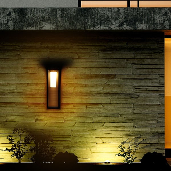 Beleuchtete Wand mit einer modernen Außenwandleuchte und Pflanzen im Garten.