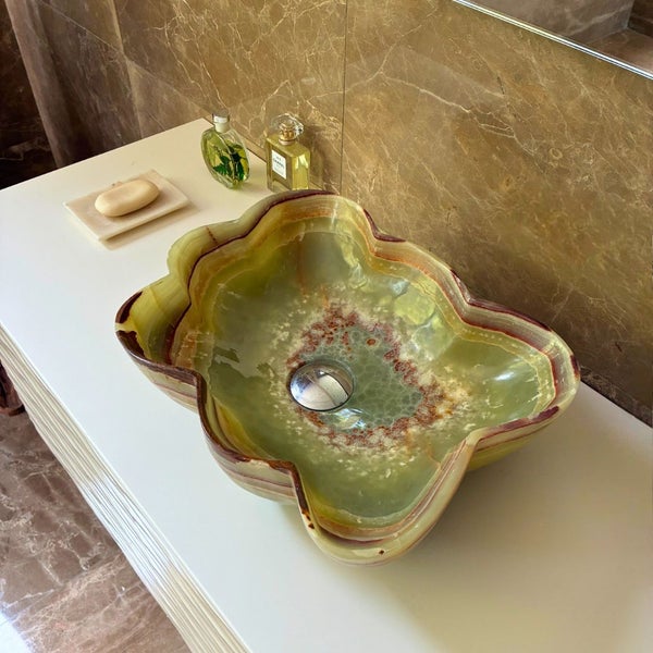 Blumenförmiges Aufsatzwaschbecken aus grünem Onyx-Naturstein auf einer weißen Waschtischplatte in einem Badezimmer mit Marmorwänden.