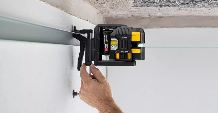 Stabila Linienlaser mit grüner Laserlinie an einer Wand befestigt während der Montagearbeiten durch eine Person.
