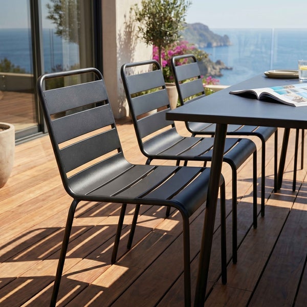 Moderne Gartenstühle und Gartentisch aus Metall auf einer Holzterrasse mit Blick auf das Meer.
