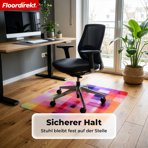 Bunte Bodenschutzmatte mit Karomuster unter einem Bürostuhl in einem hellen Arbeitszimmer mit Holztisch und Pflanzen. Floordirekt Logo.