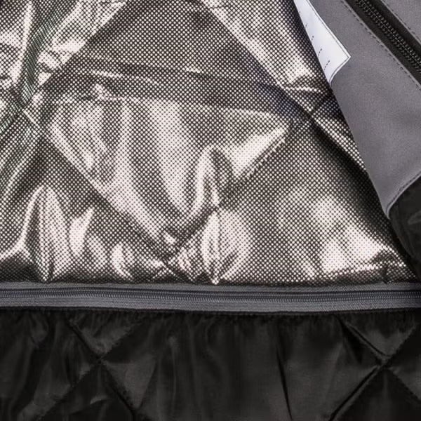 Innenansicht einer Arbeitsjacke mit wärmereflektierendem Futter mit metallischen Punkten und einem gesteppten schwarzen Innenteil mit Reißverschluss.