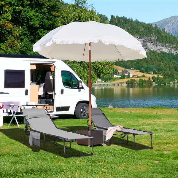 Szene mit zwei Liegestühlen, einem Sonnenschirm und einem Wohnmobil im Freien.