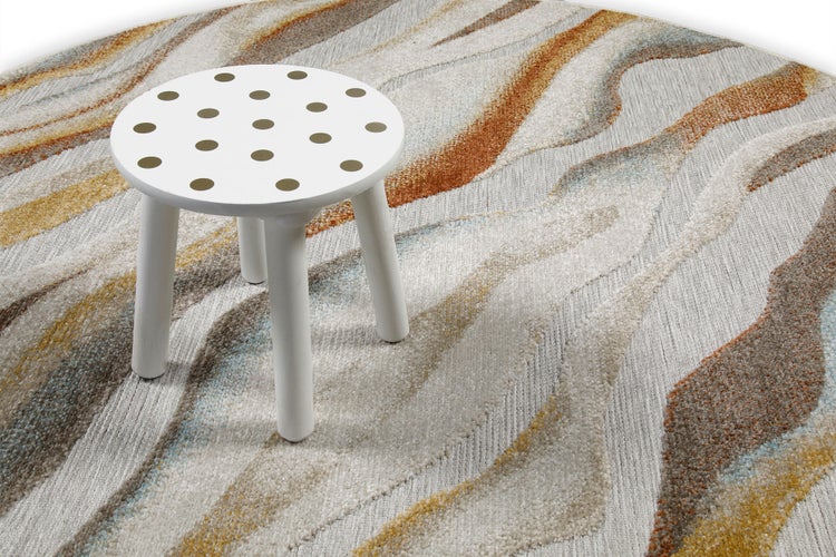 Teppich mit abstraktem Wellenmuster in Erdtönen und ein kleiner weißer Hocker mit Punkten.