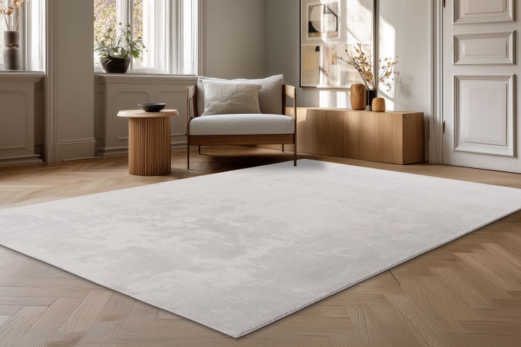 Heller moderner Wohnzimmerteppich auf Parkettboden in einem elegant eingerichteten Raum mit Sessel und Holzmöbeln.