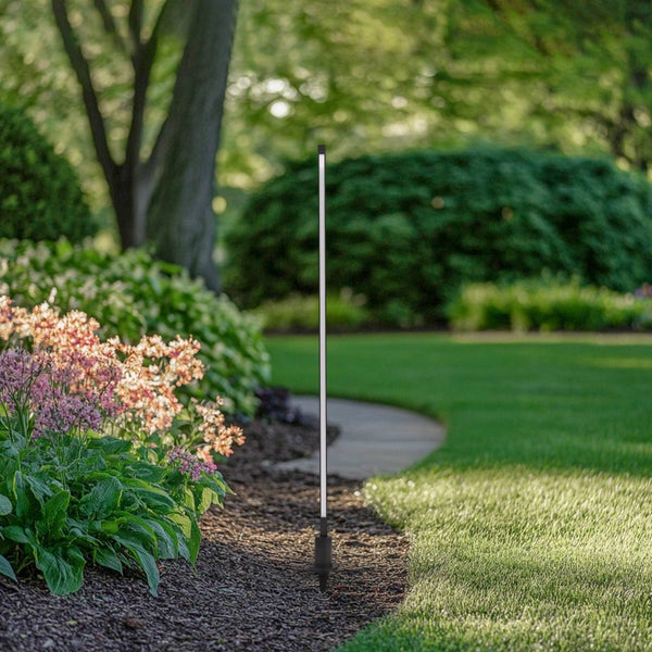 Schlanke LED-Gartenleuchte mit Erdspieß in einem gepflegten Garten mit Blumenbeet und Rasenfläche.