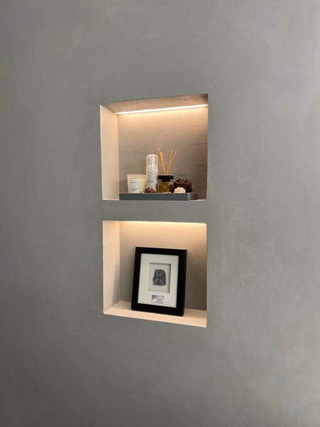 Zwei beleuchtete Wandnischen in einer glatten Wand mit Dekoartikeln und einem gerahmten Bild als moderne Wandgestaltung.