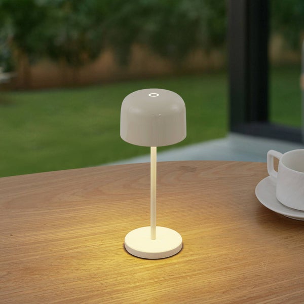 Moderne tragbare LED Tischleuchte mit abgerundetem Schirm auf einem Holztisch im Außenbereich.