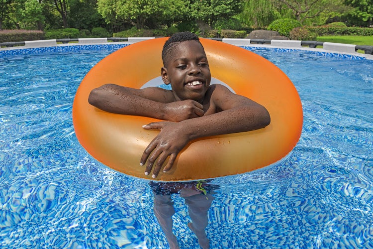 Ein Kind mit einem orangefarbenen Schwimmreifen in einem hellen Aufstellpool mit blauem Mosaikmuster.