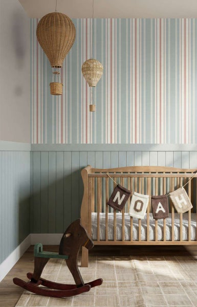 Kinderzimmer mit gestreifter Tapete, Holzgitterbett mit Namensgirlande und Schaukelpferd vor einer getäfelten Wand mit hängenden Heißluftballons.