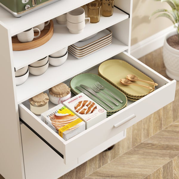 Hell gestalteter, organisierter weißer Küchenschrank mit offener Schublade und Regalen, bestückt mit Geschirr, Besteck und Backmischungen.
