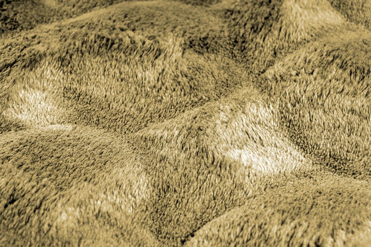 Strukturaufnahme einer weichen, kuscheligen Wohndecke aus Kunstfell mit einer dichten, flauschigen Oberfläche.