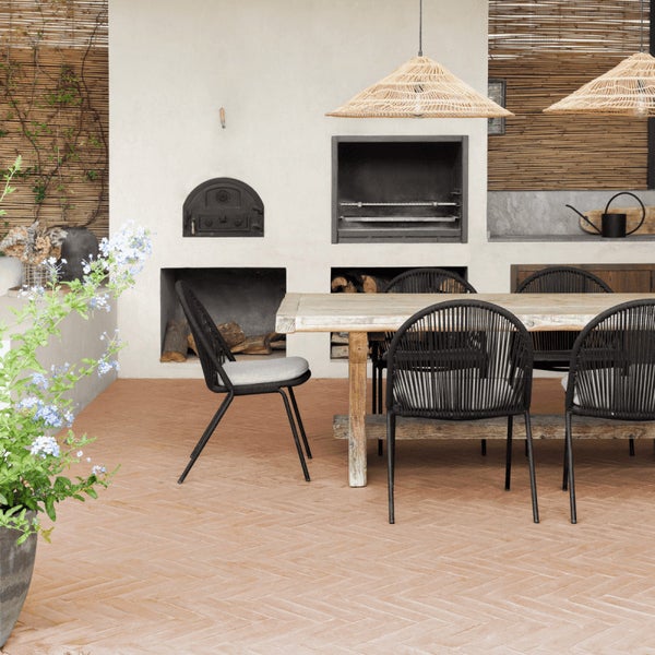 Überdachte Außenterrasse mit gemauertem Grill, Holztisch und modernen Gartenstühlen in natürlichem Ambiente.