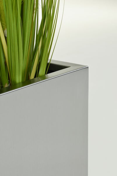 Nahaufnahme einer Ecke eines silberfarbenen rechteckigen Pflanzkübels mit künstlichem grünen Gras.