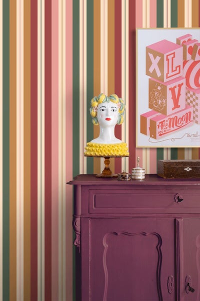 Gestreifte Tapete mit bunten vertikalen Streifen hinter einer lila Kommode mit dekorativer Büste und gerahmtem Poster im eklektischen Stil.
