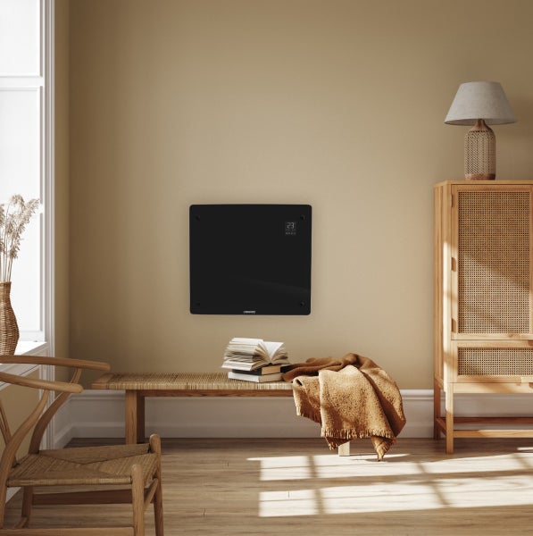Ein elektrisches Glasheizpaneel der Marke Vonroc, wandmontiert in einem modern eingerichteten Wohnraum mit Holzmöbeln und gemütlicher Dekoration.