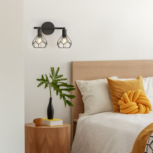 Wandleuchte mit zwei Leuchten und geometrischem Lampenschirm über einem Nachttisch in einem Schlafzimmer.