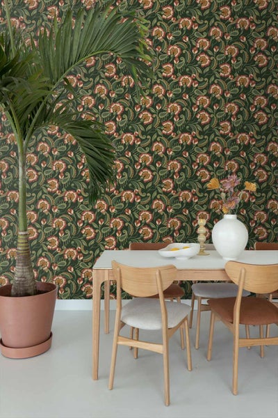 Modernes Esszimmer mit einer dunkelgrünen Vliestapete mit Blumen- und Paisleymuster, Holztisch, Stühlen und einer großen Palme im Topf.