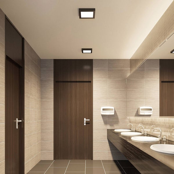 Modernes Badezimmer mit vier weißen Waschbecken auf einem dunklen Holztisch, beigen Wandfliesen und zwei quadratischen Deckenleuchten.