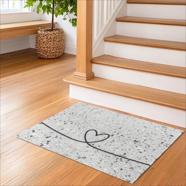 Rechteckige Fußmatte mit Herz-Motiv auf Holzboden vor einer Treppe in einem hellen Eingangsbereich.