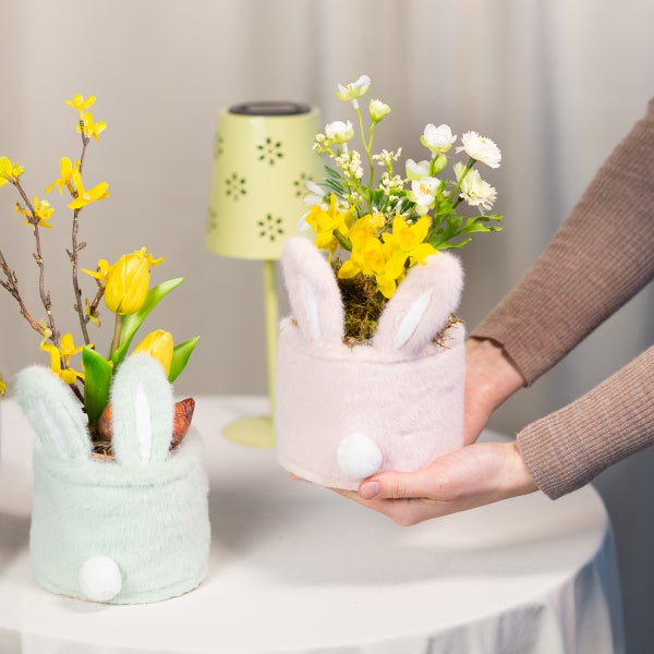 Dekorative Blumentöpfe in Hasenform mit Frühlingsblumen auf einem Tisch