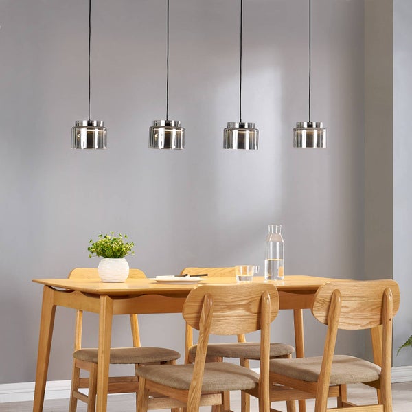 Vier moderne Pendelleuchten mit Glasschirmen und Chrom-Elementen über einem Esstisch aus Holz mit Stühlen in einem hellen Esszimmer.
