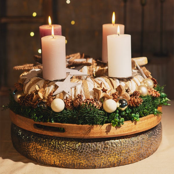 Dekorativer Adventskranz mit brennenden Kerzen, Sternen und Kugeln auf einem Holztablett