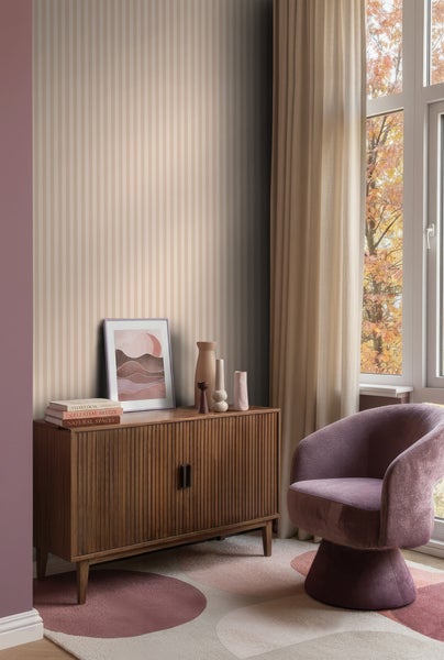 Vliestapete mit vertikalen Streifen in Beige und Hellbraun in einem modern eingerichteten Wohnzimmer mit Sideboard und Sessel.
