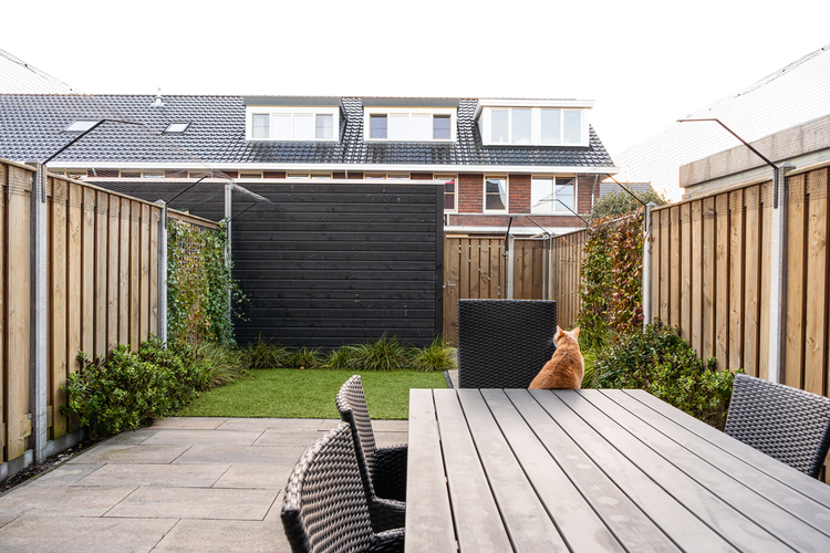 Moderner Garten mit Holzzäunen, Steinterrasse, Holztisch, Rattanstühlen, Kunstrasen und Katzennetz-System zur Absicherung.