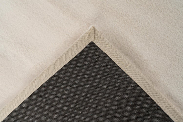 Nahaufnahme einer Teppichecke mit weicher Oberseite, strukturierter Rückseite und eingefasster Kante.