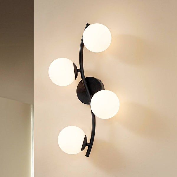 Wandleuchte mit vier runden, leuchtenden Glaskugeln und schwarzem Metallgestell an der Wand.