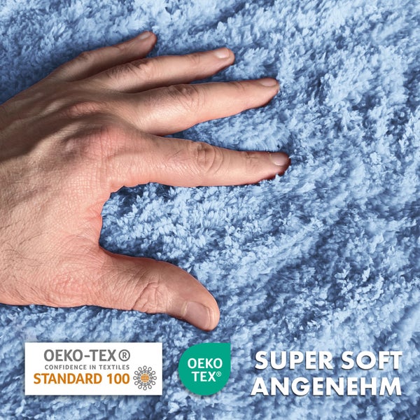 Hand auf blauem Badteppich mit Öko-Tex Siegel und Aufschrift Super Soft Angenehm.