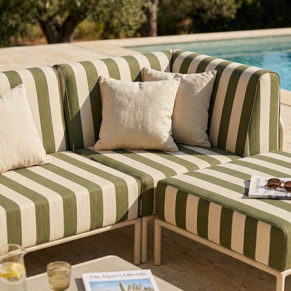 Modernes Outdoor-Loungesofa mit gestreiften Polstern und hellen Kissen auf einer Terrasse neben einem Pool.