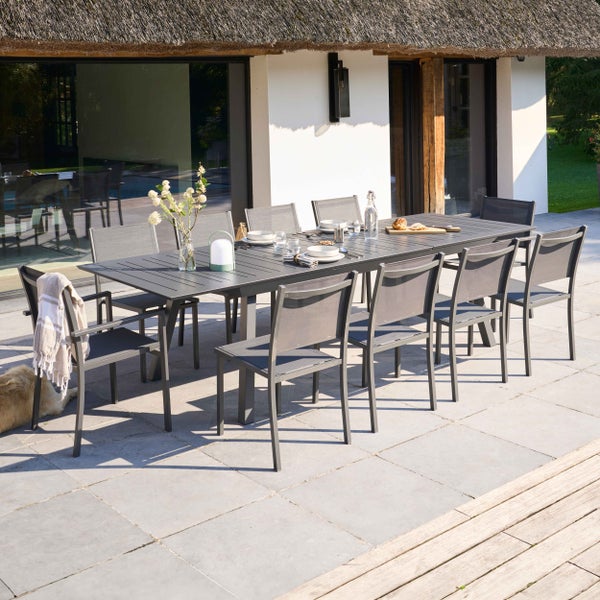 Moderne Garten-Essgruppe aus Metall mit großem Tisch und Stapelstühlen auf einer Steinterrasse in einer hellen, organisierten Umgebung.