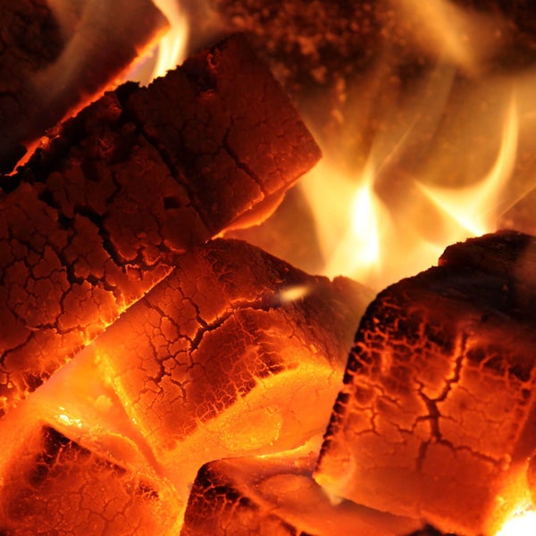 Brennholz oder Holzbriketts in Flammen, glühende Glut mit sichtbarer Oberflächenstruktur und lodernden Flammen.