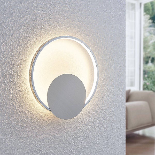 Moderne LED-Wandleuchte aus Metall in kreisförmigem Design mit indirekter, warmer Beleuchtung an einer strukturierten Wand.