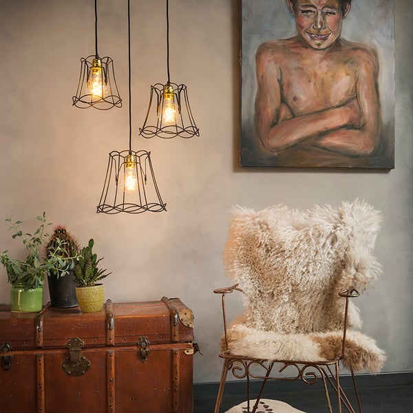 Raumansicht mit drei Pendelleuchten, Sessel mit Schaffell, Koffer und Gemälde