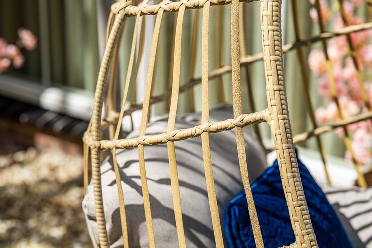 Detailaufnahme eines Hängesessels aus Polyrattan-Geflecht mit Sitzkissen im Garten.