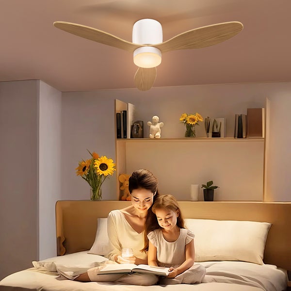 Deckenventilator mit drei Holzflügeln und integrierter Lampe in einem hellen Schlafzimmer über einem Bett mit einer lesenden Mutter und Tochter.