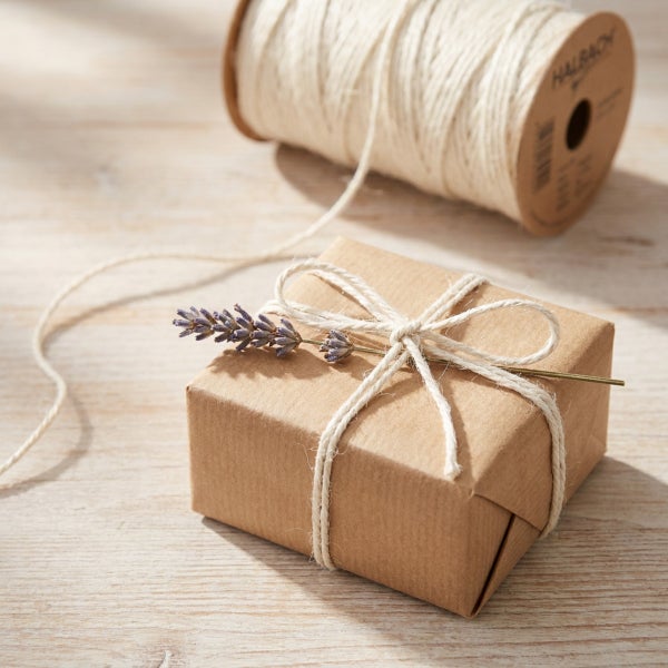 Geschenk verpackt in braunem Papier mit einer Schnur aus Baumwolle und einem Zweig Lavendel auf einem Holztisch.